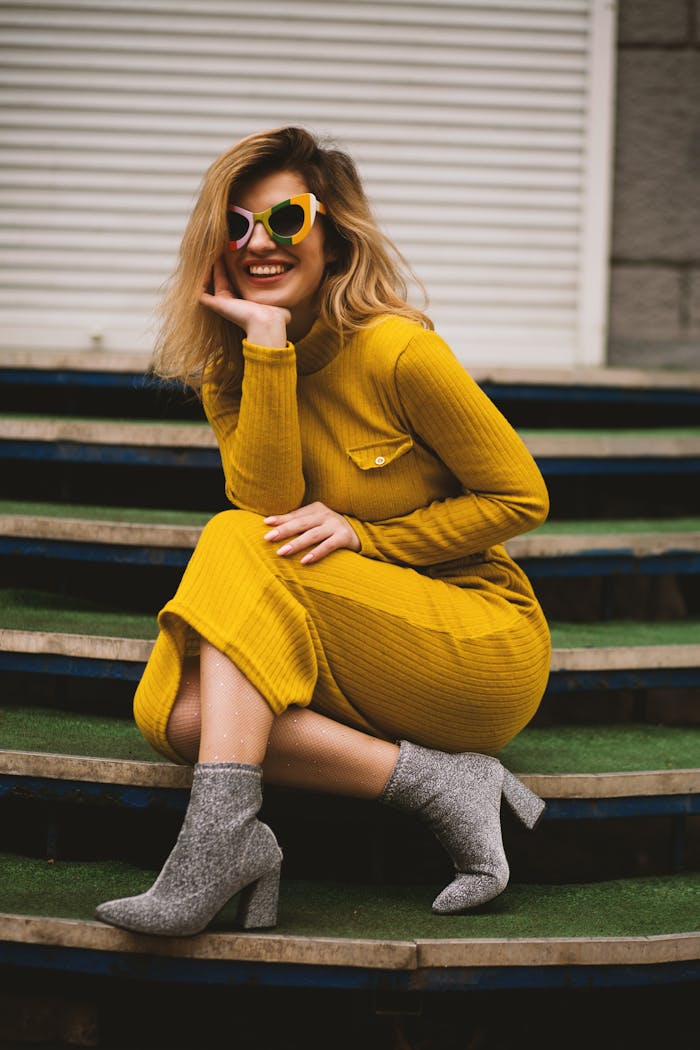 Stylish woman in yellow dress and sunglasses posing on steps. Modern fashion portrait.