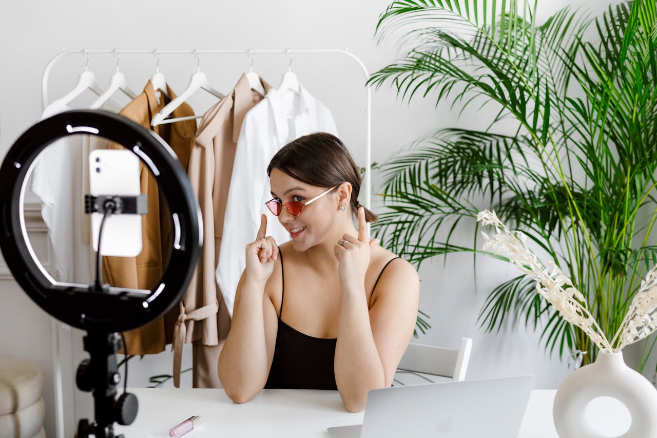 Stylish woman vlogging with ring light, surrounded by fashion accessories and greenery.